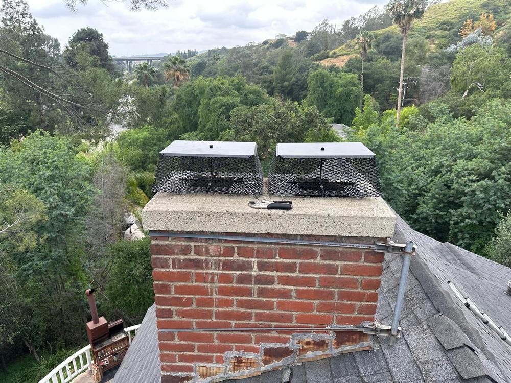 Two newly fitted stainless steel chimney caps with spark arrestor mesh on a brick chimney above a Sacramento-area rooftop